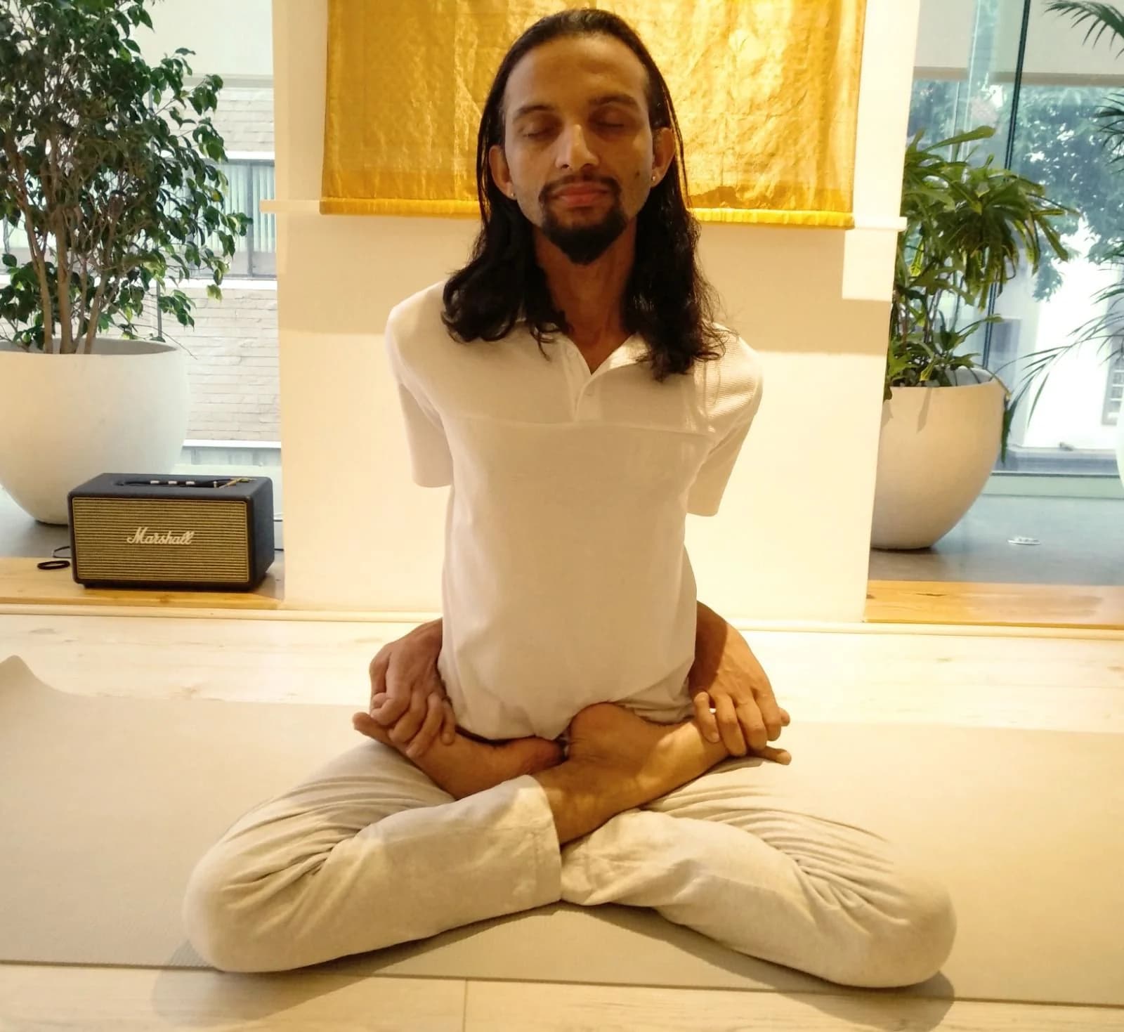 Swami G in white, seated in bound lotus pose with his eyes closed